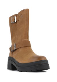 Bottines en cuir marron avec une semelle noire épaisse, des boucles en métal réglables et des détails de couture sur les côtés.