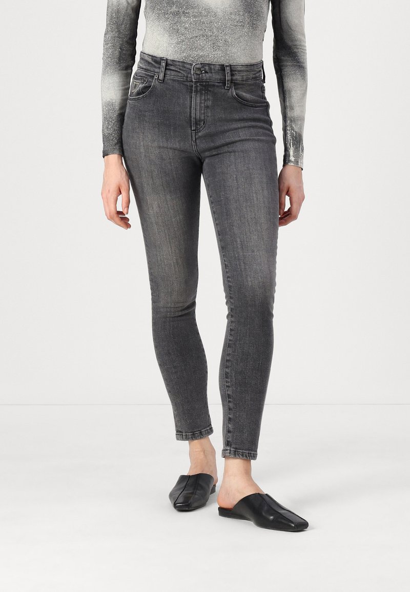 Jean en denim gris slim fit avec texture décolorée, taille haute et design à cinq poches, associés à des chaussures noires à enfiler.