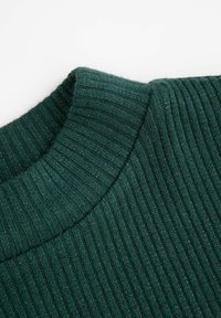 Zbliżenie na prążkowaną dzianinę w ciemnozielonym kolorze, skupiające się na złożonym kołnierzu typu golf i teksturowanym wzorze szwów.