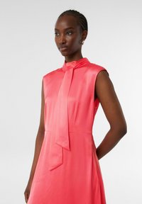 Satin ärmelloses Kleid in leuchtendem Korallenrot, mit einem gebundenen Kragen und einer glatten, fließenden Silhouette. Keine sichtbaren Muster oder Beschläge.