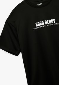 Czarny t-shirt z krótkim rękawem, wykonany z gładkiego materiału, z wyraźnym białym napisem: "URODZONY GOTOWY" oraz "PRZYGOTOWANIE TO MOJE DOMYŚLNE USTAWIENIE."
