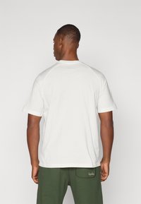 Hvid bomulds T-shirt med korte ærmer og rund halsudskæring, der har en glat tekstur. Bagud fra T-shirten ses en afslappet pasform og et simpelt design.