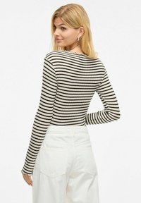 Zwart-wit gestreepte langwerpige top met geribbelde textuur, geschulpte kraag, gecombineerd met witte high-waisted broek. Achteraanzicht.