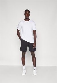 T-shirt blanc à manches courtes et shorts de sport noirs avec logo sur l'ourlet. Baskets blanches. Design simple, en coton, coupe décontractée.