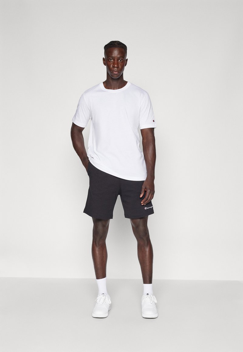 T-shirt blanc à manches courtes et shorts de sport noirs avec logo sur l'ourlet. Baskets blanches. Design simple, en coton, coupe décontractée.
