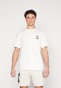 Κρεμ καμπαρντίσα μπλούζα από βαμβάκι με κοντά μανίκια, με λογότυπο Adidas σε μαύρο χρώμα και κείμενο "Star Wars" στο αριστερό στήθος.