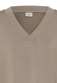 Chemise beige à col en V avec une étiquette de marque Fransa visible cousue à l'intérieur du col, montrant une texture de tissu lisse.