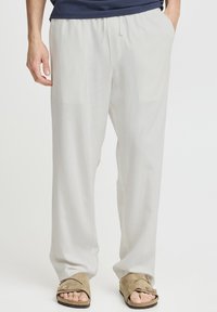 Letvægts, hvide linnedbukser med elastisk taljebånd, to sidelommer og en afslappet pasform, kombineret med beige slide-sandaler.