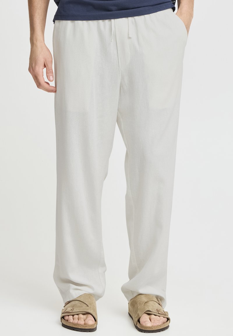 Letvægts, hvide linnedbukser med elastisk taljebånd, to sidelommer og en afslappet pasform, kombineret med beige slide-sandaler.