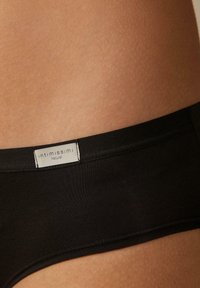 Zwarte katoenen bikini ondergoed met een gladde textuur, voorzien van een logo-label op de tailleband. Close-up van de stof en naden.