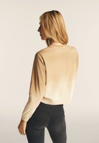 Felpa beige con gradiente, maniche lunghe e scollatura rotonda. Il tessuto sembra morbido con una texture liscia, con una lunghezza accorciata alla vita.