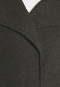 Primo piano del colletto di un cappotto di lana grigio scuro sopra un maglione di cotone bianco, che mette in evidenza la texture del tessuto e il design del rever.
