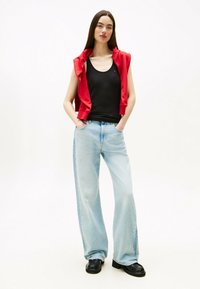 Top in cotone nero, felpa senza maniche rossa, jeans a gamba larga blu chiaro e scarpe con platform nere. Tessuto morbido, vestibilità rilassata e linee pulite.