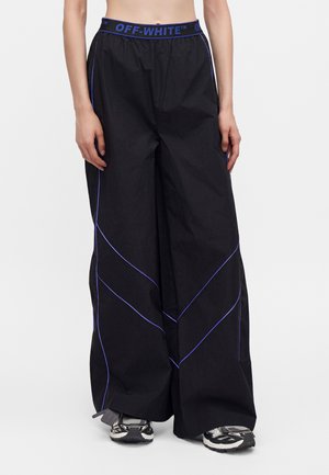 Sorte bukser med vide ben med blå piping og en elastisk talje med Off-White-mærke, båret med sorte og hvide sneakers.