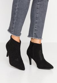 Botas de terciopelo negro hasta el tobillo con pequeños remaches, punteras afiladas, cremalleras laterales, combinadas con unos vaqueros oscuros recortados y deshilachados.