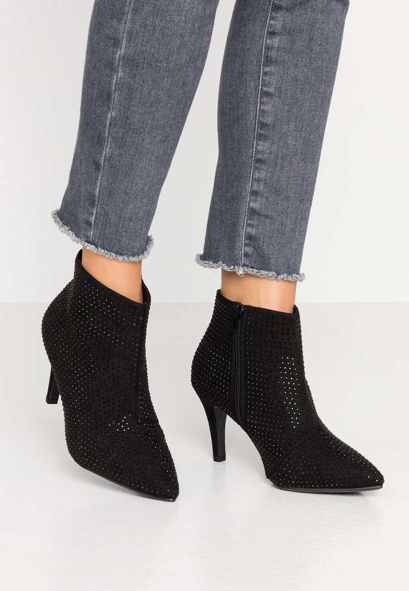 Botas de terciopelo negro hasta el tobillo con pequeños remaches, punteras afiladas, cremalleras laterales, combinadas con unos vaqueros oscuros recortados y deshilachados.