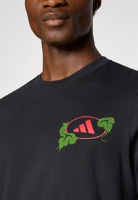 Sort bomulds T-shirt med et centralt grafisk motiv af røde former med grønne vin-detaljer. Rund hals og korte ærmer.