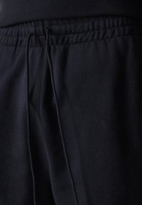 Sorte idrettsbukser laget av myk stoff, med elastisk midje og snor, har lommer på sidene og en glatt tekstur.