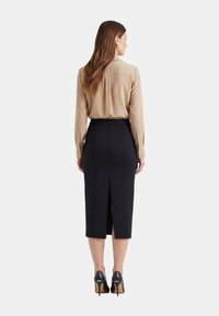 Blusa beige a maniche lunghe con polsini con bottoni abbinata a una gonna nera al ginocchio con spacco posteriore. Scarpe nere con tacco alto completano il look.