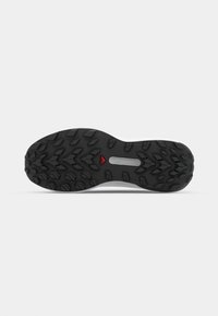 Semelle extérieure en caoutchouc noir avec un motif de crampons multidirectionnel, mettant en avant un accent rouge central. Texture lisse avec une forme profilée pour une bonne adhérence.