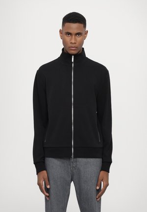 Black zip-up jacket with a high collar, made of soft material. Features a smooth texture and side pockets, paired with gray jeans.