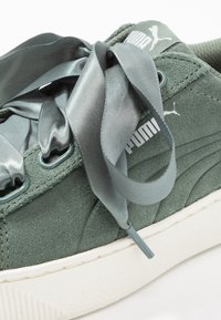 Grüne Wildleder-Sneaker mit einer dicken weißen Sohle, ausgestattet mit Satinschnürsenkeln und Puma-Branding an der Seite mit strukturierter Oberfläche.