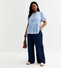 Blaue und weiße karierte Bluse mit puffigen Ärmeln, gebundenem Ausschnitt und Peplum-Saum, kombiniert mit weit geschnittenen dunklen Jeans und beigen Sneakers.