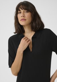 Top nero a maglia con scollo a V e maniche corte. Texture liscia e design minimale, con un colletto sottile e una vestibilità morbida.