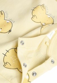 Dzeltena bērnu apģērba gabals ar vistas druku, mīksts audums, ribotās piedurknes un snap aizdares. Ietver rotaļīgu dizainu ar gaišiem akcentiem.