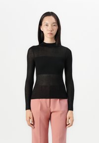 Musta ribbed pitkähihainen paita, jossa on mock neck -kaulus. Ominaisuuksiin kuuluu raidallinen pinta, hieman läpikuultava malli, yhdistettynä vaaleanpunaiseen muotihousupariin.