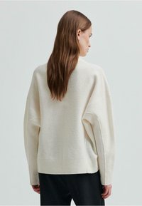 Maglione oversized di colore crema realizzato in un tessuto morbido e testurizzato, con orlo a coste e maniche ampie. Presenta una vestibilità rilassata e un design minimalista.