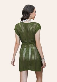 Abito lavorato a maglia verde oliva, maniche corte con motivo a maglia aperta, vita stretta e lunghezza sopra il ginocchio. Legami bianchi accentuati al collo.