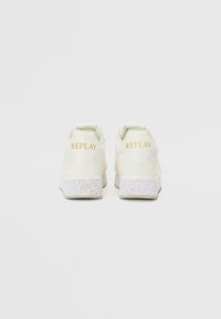 Zapatillas de color crema con un acabado texturizado, que presentan un logo dorado "REPLAY" en el talón y suelas blancas salpicadas.