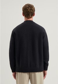 Černý pletený svetr s žebrovaným límcem a lemem, s jemnou texturou a uvolněným střihem, z pohledu zezadu.