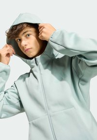 Sudadera con capucha y cremallera en azul claro con acabado texturizado y bolsillos delanteros. Presenta un logo sutil en la parte superior izquierda.