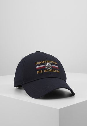 Casquette de baseball bleu marine avec logo Tommy Hilfiger, bande rouge, blanche et bleue, et texte brodé en or indiquant "TOMMY HILFIGER EST. MCMLXXXV".
