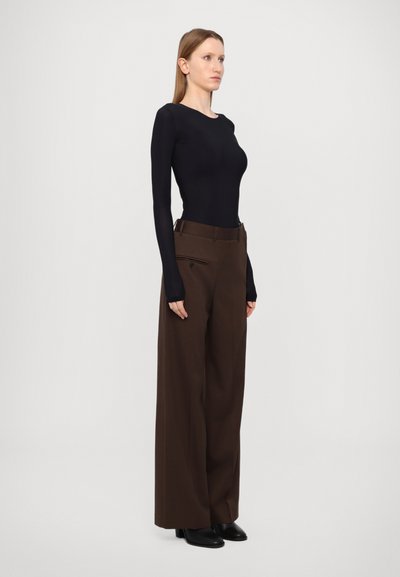 Black long-sleeve fitted top paired with wide-leg brown trousers. Trousers feature a zipper pocket detail, worn with black heeled boots.