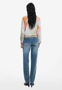 Bunter Pullover mit einem Batikmuster, kombiniert mit hellblauen Jeans. Das Outfit hat eine lockere Passform und eine weiche Textur.