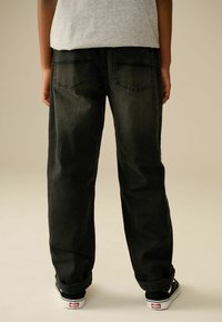 Jean en denim noir avec une coupe décontractée, dotés de deux poches arrière et de revers, associés à des chaussures noires et blanches.
