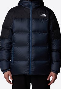 Doudoune bleu marine avec un panneau d'épaule noir, fermeture éclair et capuche. Comprend des sections matelassées, des poches latérales et un logo sur la poitrine.