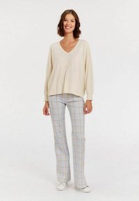 Pull crème en V avec une coupe ample et des manches longues, associé à un pantalon à carreaux bleu et jaune et des baskets blanches. Tissu texturé.