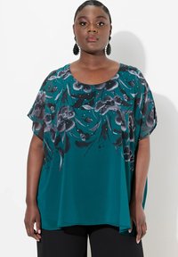 Teal bluse med blomsterprint i grå og sort, med en rund halsudskæring og korte, brede ærmer. Glat stof med let drapering.