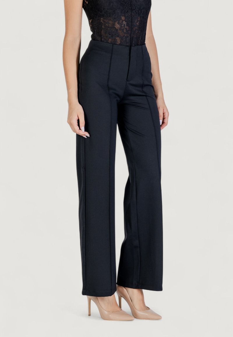 Pantaloni neri a vita alta con una vestibilità su misura; pieghe lungo la parte anteriore; tessuto liscio; indossati con décolleté color carne.