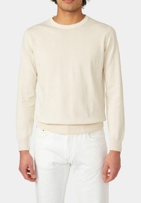 Licht beige gebreide trui met een ronde halslijn, geribbelde manchetten en rand, getailleerde pasvorm en een gladde textuur. Gecombineerd met witte broeken.