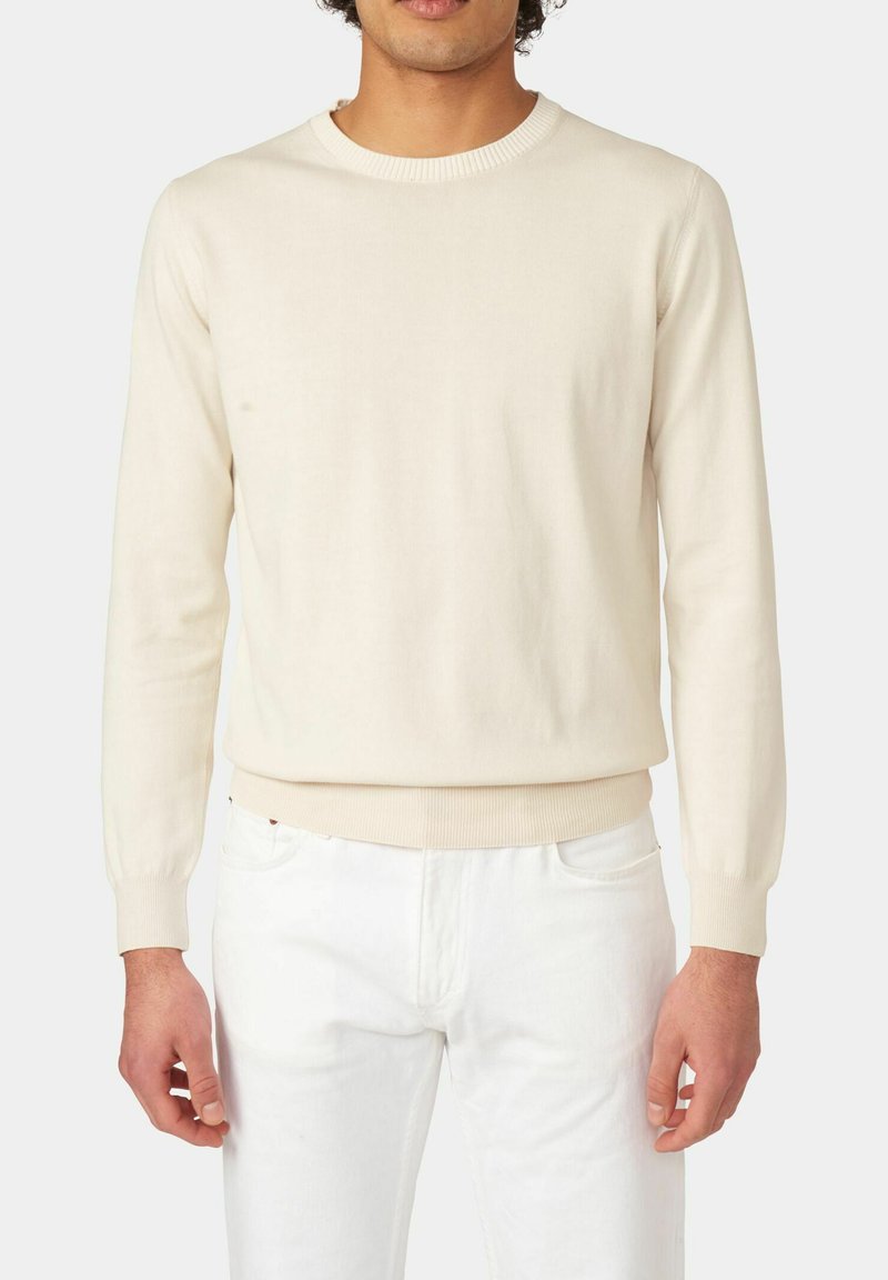 Licht beige gebreide trui met een ronde halslijn, geribbelde manchetten en rand, getailleerde pasvorm en een gladde textuur. Gecombineerd met witte broeken.