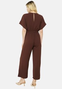 Bruine jumpsuit met korte mouwen, een getailleerde taille en brede pijpen. Voorzien van een keyhole-ontwerp aan de achterkant. Soepele textuur, casual pasvorm, minimalistisch ontwerp.