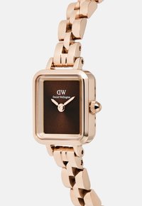 Montre-bracelet en or rose avec un boîtier rectangulaire, un cadran marron et un bracelet en métal à maillons. Présente des index horaires minimalistes et une couronne.