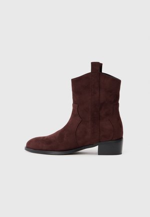 Stivaletti alla caviglia in suede bordeaux con punta rotonda, tacco basso a blocco e un dettaglio di cucitura decorativa lungo i lati. Nessun hardware visibile.