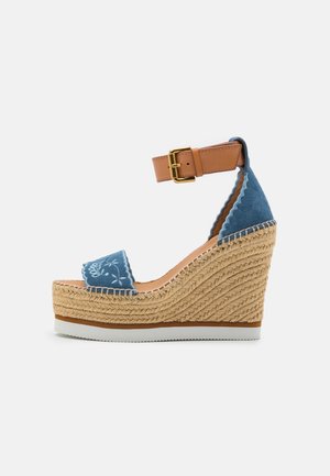 Sandale compensée en daim bleu avec bride marron à la cheville, broderie florale blanche et semelle plateforme en jute tressée.