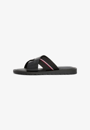 Svart sandal med kryssende remmer, laget av glatt lær og elastisk stoff med en rød, hvit og blå stripe, teksturert såle.